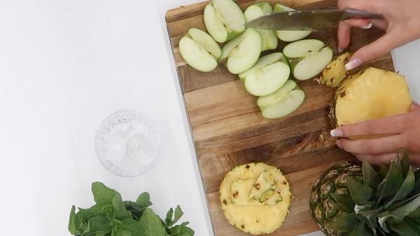 green juice recipe with wooden chopping board, pineapple, apples, mint and a glass